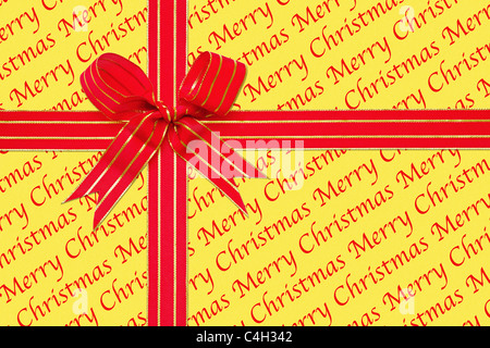 Photo of a gift wrapped in Merry Christmas paper with a red and gold ribbon tied in a bow. Stock Photo
