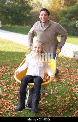 Father pushing child through autumn leaves on wheelbarrow Stock Photo
