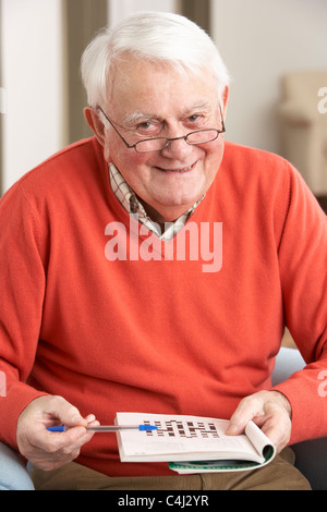 Senior Man Relaxing In Chair At Home Completing Crossword Stock Photo