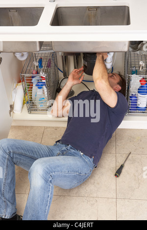 Plumber Working On Sink In Kitchen Stock Photo