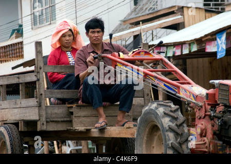 A man and a woman who are hilltribe subsistence farmers are riding on a tractor in rural communist Laos. Stock Photo