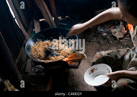 An Asian woman living in poverty is frying rice in a pan on a wood burning stove in communist Laos. Stock Photo