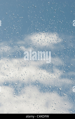 Raindrops on a window in front of a cloudy blue sky Stock Photo