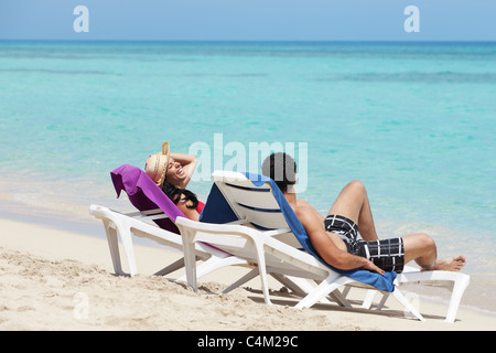 husband and wife relaxing on sunbeds on the beach and smiling. Horizontal shape, side view, copy space Stock Photo