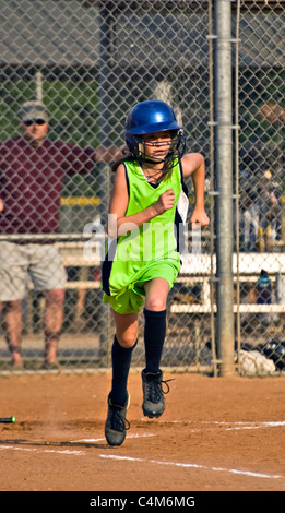 A preteen girl running to first base after making a hit, her coach watching. Stock Photo