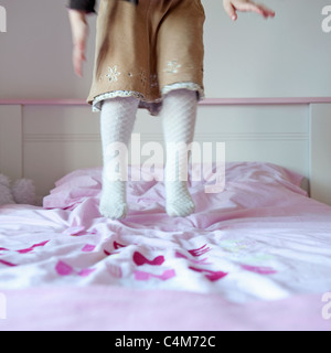 3 year old girl wearing a brown kirt and tights jumping on her pink bed. Stock Photo