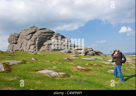 A photographer taking pictures of Haytor rocks in Dartmoor National Park with people climbing the rock for the fantastic views. Stock Photo