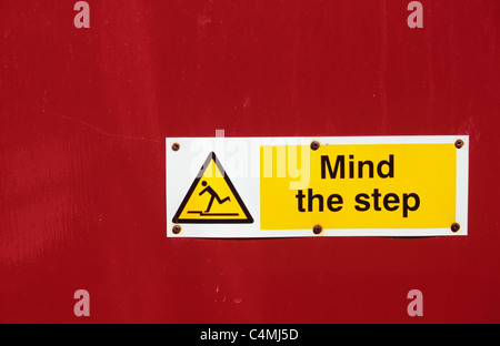 Red door with yellow black and white safety sign stating Mind the Step with icon of man tripping Stock Photo