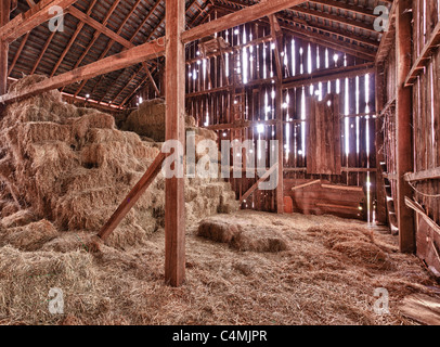 Old Barn with the sun streaming from outside and straw and hay on the floor of the hayloft Stock Photo