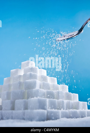 a studio shot of a sugar cube pyramid with sugar falling on to it from a spoon, with blue background Stock Photo