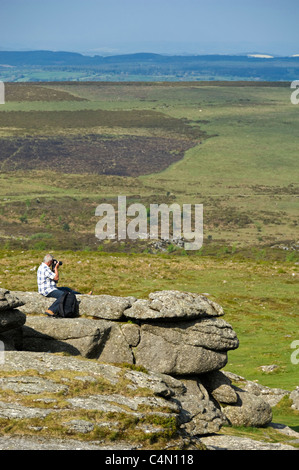 Vertical wide angle of a man taking photographs of the view from Haytor or Hay Tor, on Dartmoor National Park on a summer's day. Stock Photo