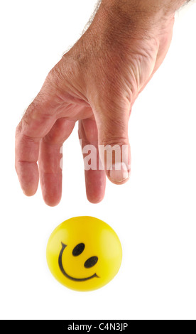Mans hand grabbing  a yellow smiley rubber ball. Stock Photo