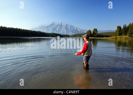 Middle age male fly fishing in mountain lake. Two Jack Lake with Rundle Mountain background, Banff National Park, Alberta, Canad