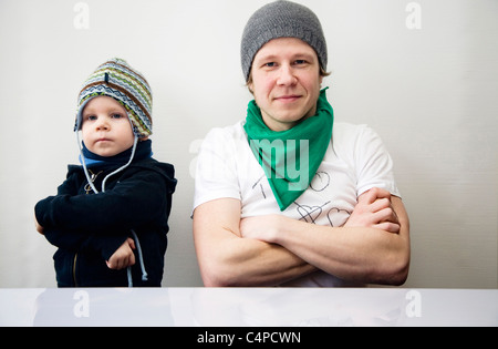 Father and son with folded arms sitting at a table, Germany Stock Photo