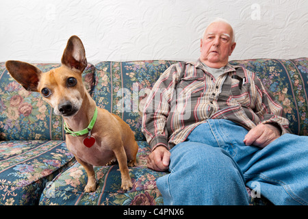A retired elderly Senior Man in his home sitting on his couch with his dog by his side. Stock Photo