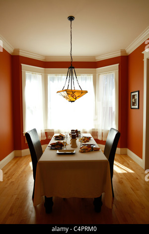 Sun shines in through the window of a formal dining room with red walls and wood floor. Stock Photo