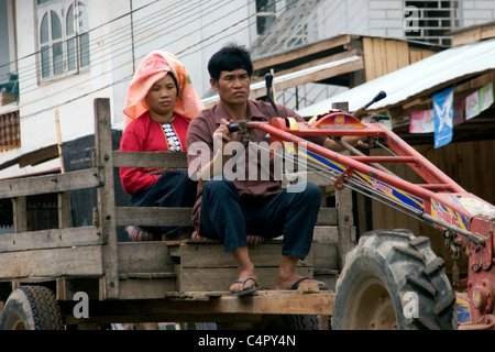 A man and a woman who are hilltribe subsistence farmers are riding on a tractor in rural communist Laos. Stock Photo