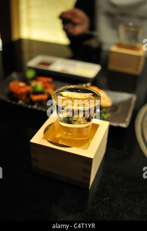 Full sake cup in a wooden box on a table in a restaurant in Tokyo Stock Photo