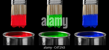 Three paint brushes dipped in red green and blue paint isolated on black background Stock Photo