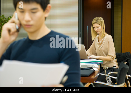 Female executive working on laptop computer, colleague in foreground Stock Photo