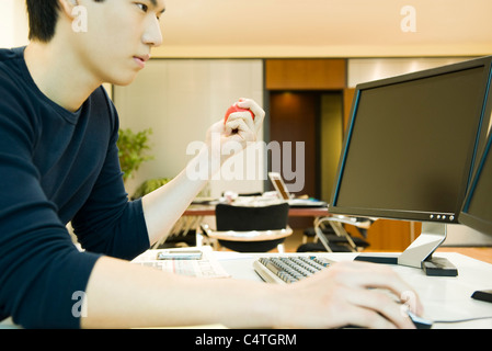 Office worker using computer, squeezing stress ball with one hand Stock Photo