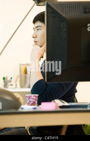 Young man sitting at desk, looking away in thought Stock Photo