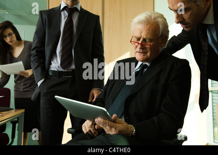 Executives looking down at digital tablet and having discussion Stock Photo