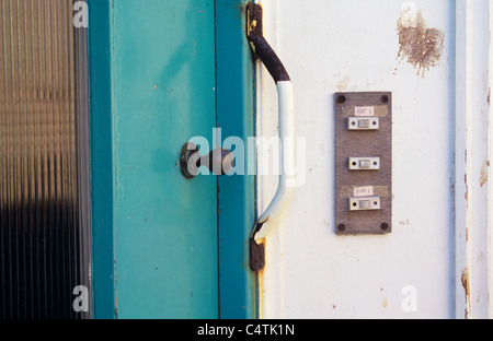 Entrance to rundown block of flats with three bell push buttons turquoise front door rusty grip handle and bird dropping Stock Photo