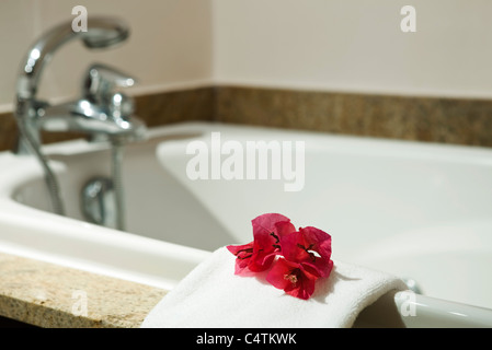 Fresh towel decorated with flower heads handing on edge of bathtub Stock Photo