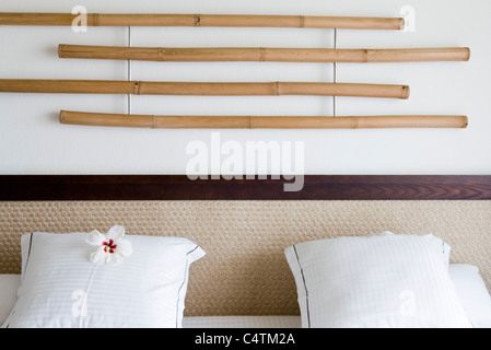 Bamboo decoration hanging on wall above headboard, white hibiscus flower head on pillow Stock Photo