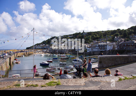 Visitors enjoy ice cream and the view on a sunny day at Mousehole harbour in West Cornwall, at low tide Stock Photo