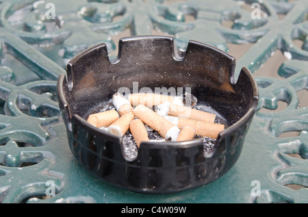 Cigarette butts in ashtray on pub garden table Uk. Smoking outside. Smoking. Health issues. Passive smoking. Stock Photo