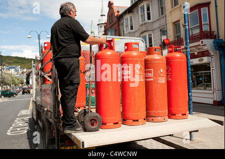 A man with a delivery of orange coloured Calor propane gas bottles cylinders, UK Stock Photo