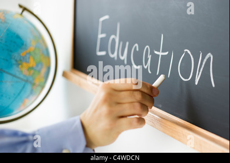 Close-up of man's hand writing 'education' on blackboard Stock Photo