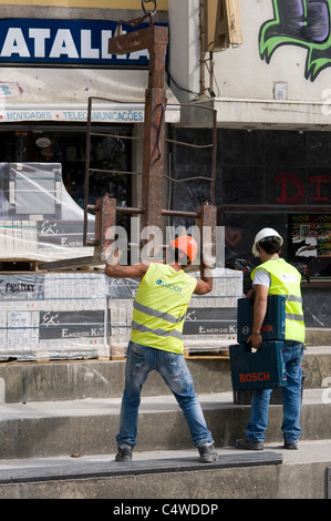 Workers in high visibility vests loading a pallet of blocks onto a crane Stock Photo