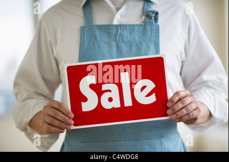Man wearing apron holding 'sale' sign,mid section Stock Photo