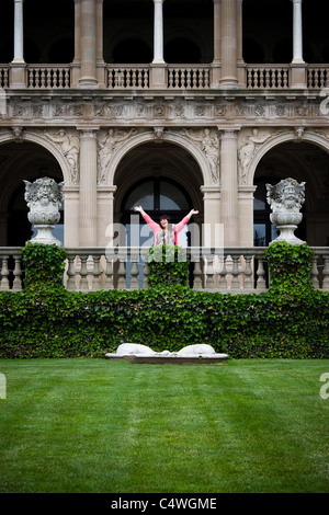 A young woman with her arms up in the air in front of a fancy mansion. Stock Photo