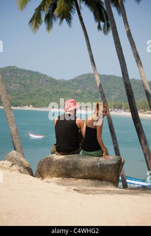 A young tourist couple sit amidst palm trees high over the ocean at Palolem Beach, in Goa state, India Stock Photo