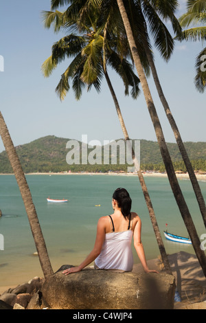 A young woman sits among palm trees high over the ocean at Palolem Beach, in Goa state, India Stock Photo