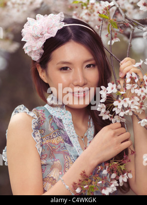 Portrait of a beautiful young smiling Asian woman standing at a blooming cherry tree in a park Stock Photo