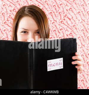 USA,New Jersey,Jersey City,Portrait of smiling young woman holding restaurant menu in front of face Stock Photo