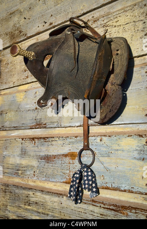 Old horse saddle hanging on an old weathered wall. Stock Photo