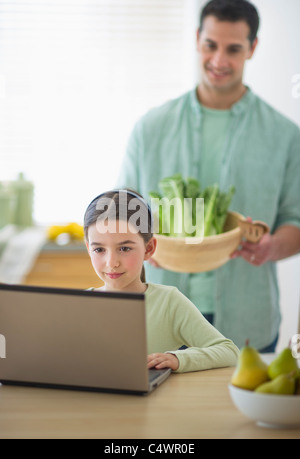 USA,New Jersey,Jersey City,girl (8-9) using laptop and father preparing food in domestic kitchen Stock Photo