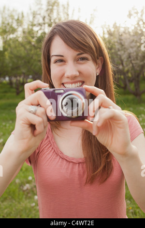 USA,Utah,Provo,Young woman holding digital camera in orchard