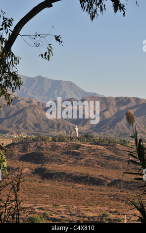 Blue sky view towards Andes of white cross on low hilltop in brown semi-desert lowland west of Cerro Gloria, Mendoza, Argentina Stock Photo