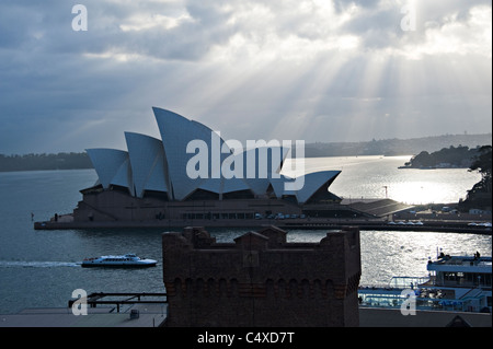 Early Morning Rays of Sunshine Pierce the Sky Over The Sydney Opera House on Bennelong Point NSW Australia Stock Photo