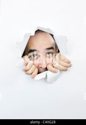 Hole in paper with scared man looking through Stock Photo