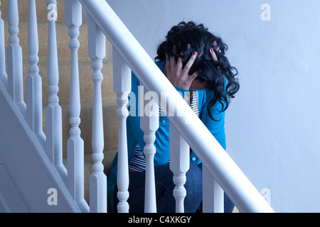 Young woman sitting alone on stairs hands on head. Stock Photo