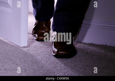Man's feet only wearing brown shoes entering a dark carpeted room Stock Photo