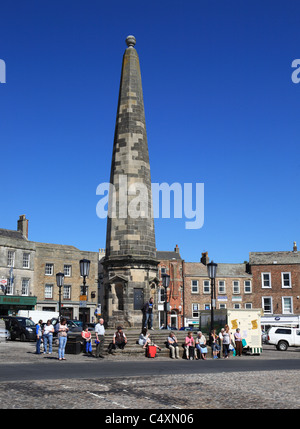 People sitting on the steps around the obelisk in Richmond's market place, North Yorkshire, England, UK Stock Photo